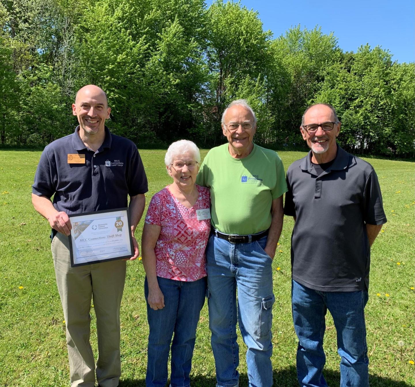 Four people pose for a photo. One is holding a framed award.