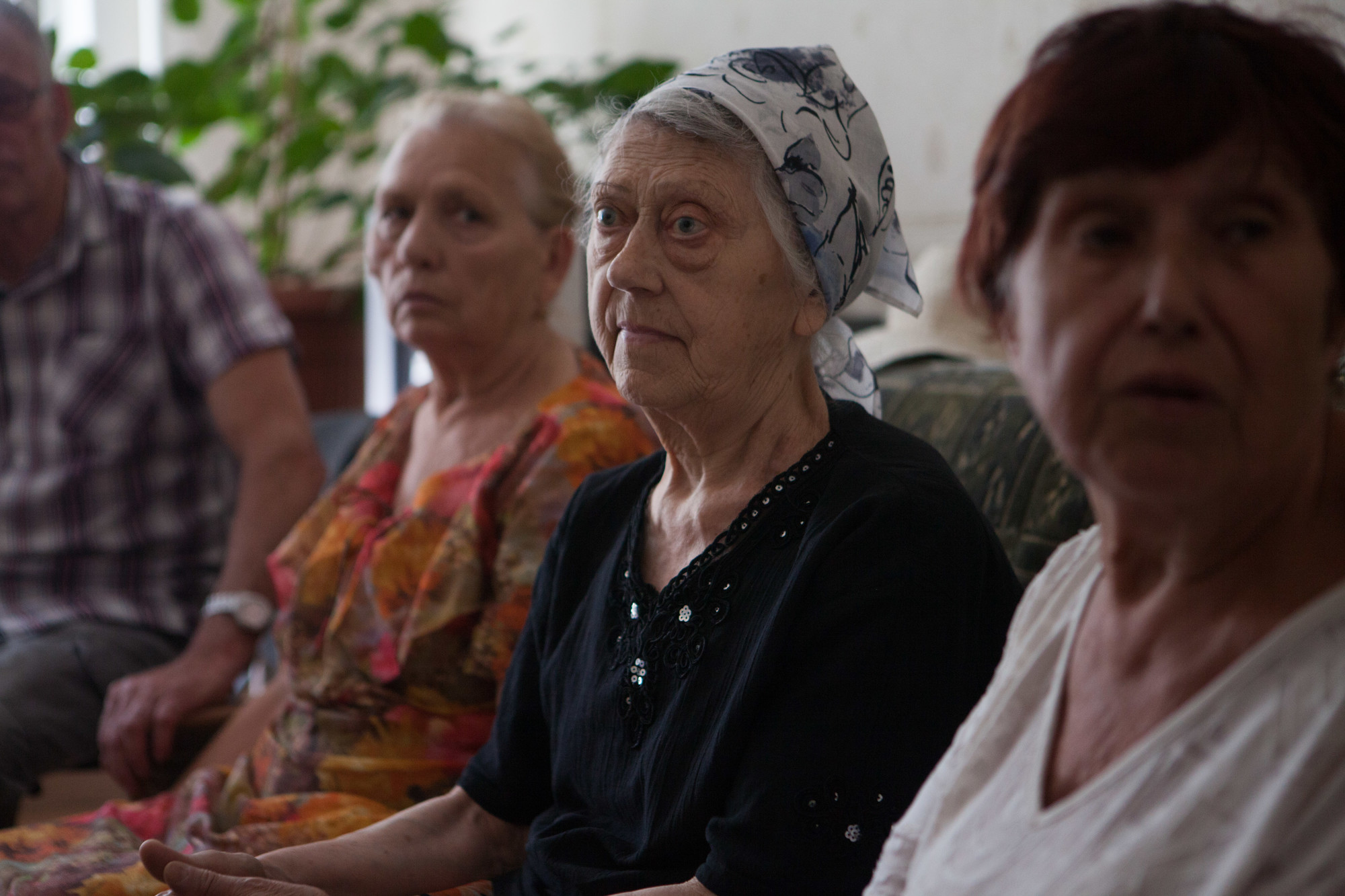 Three elder, Ukrainian women. The middle woman has a scarf on her head.