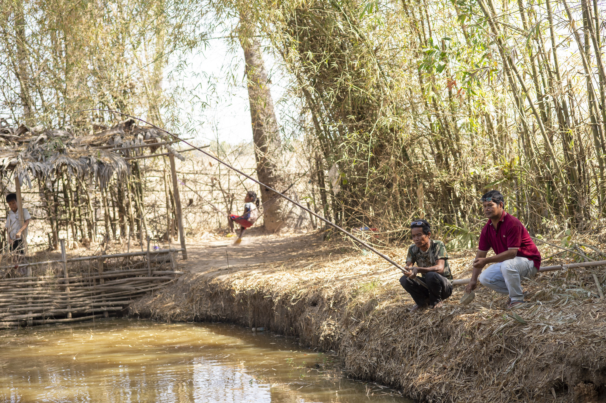 Two Cambodians fish by a small pond