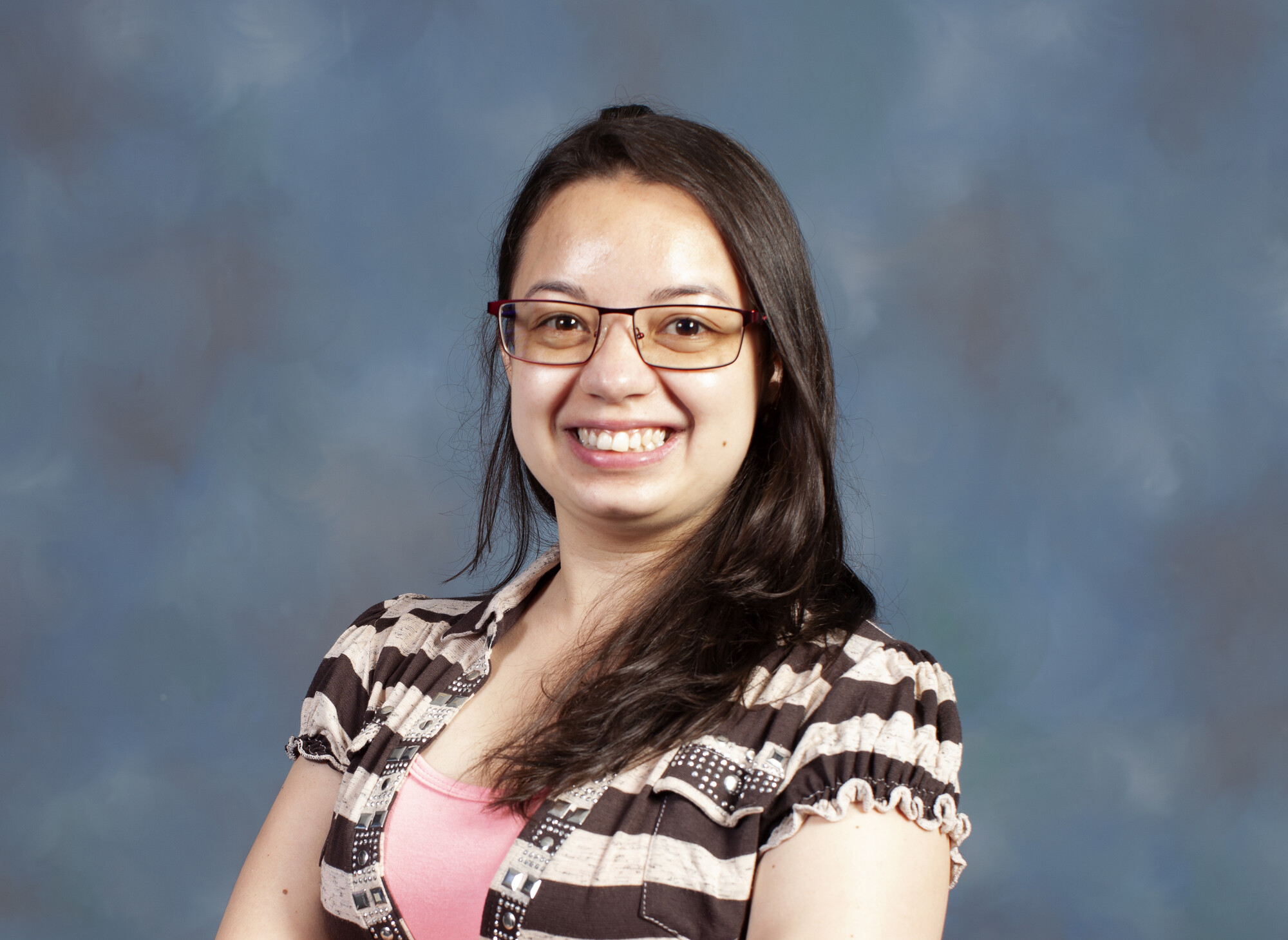 A young woman with long dark hair and glasses sits in front of a blue backdrop