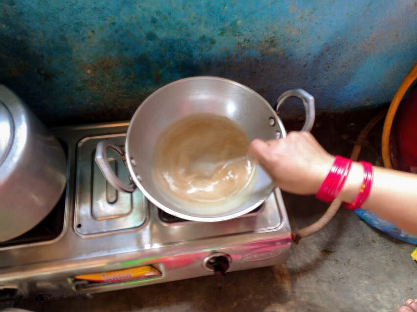 A pot cooking porridge while someone stirs it