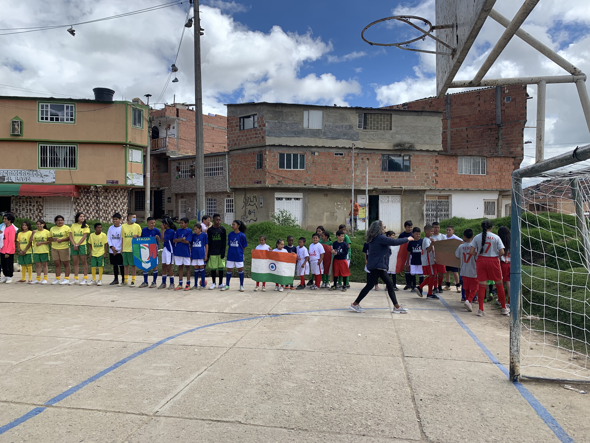 Children stand on the edge of a soccer pitch, holding country flags, in a school yard in Colombia