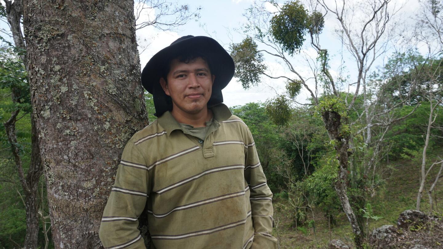 A man in a hat stands by a tree