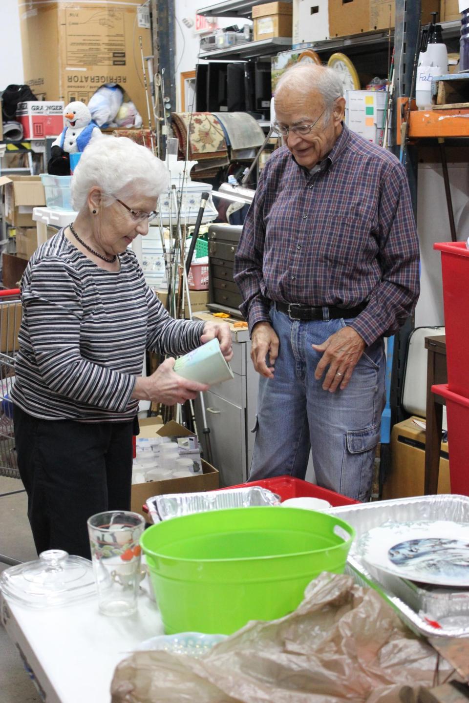 Two older people work with items in the backroom of a thrift shop