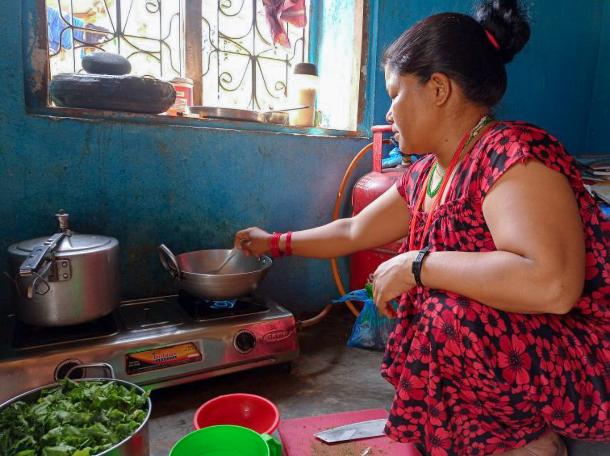 A Nepali woman squats and stirs a pot on a stove