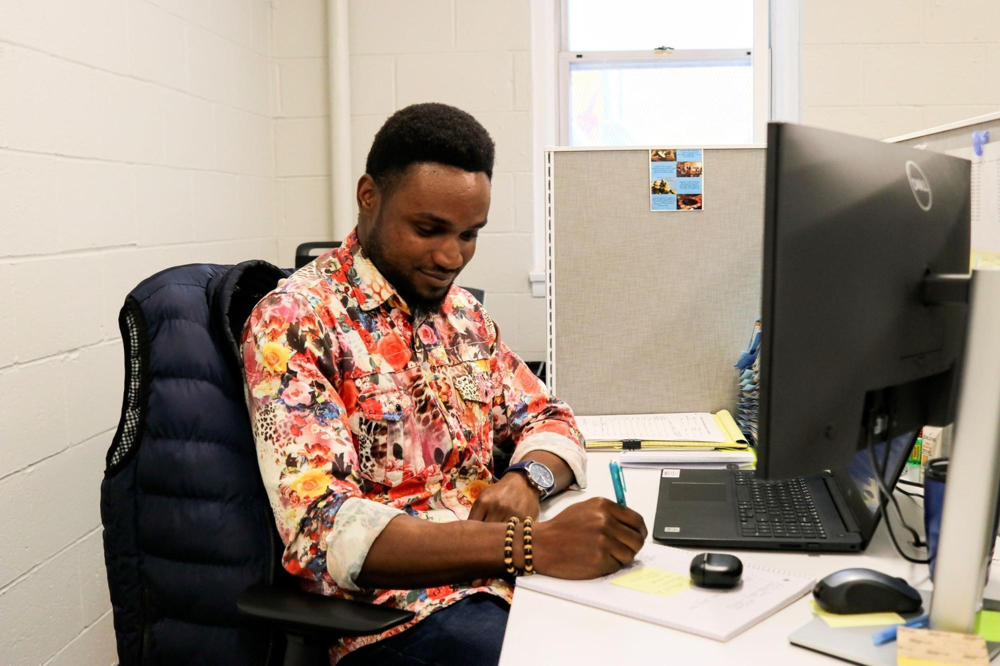 A young man in a floral shirt sits in front of a computer