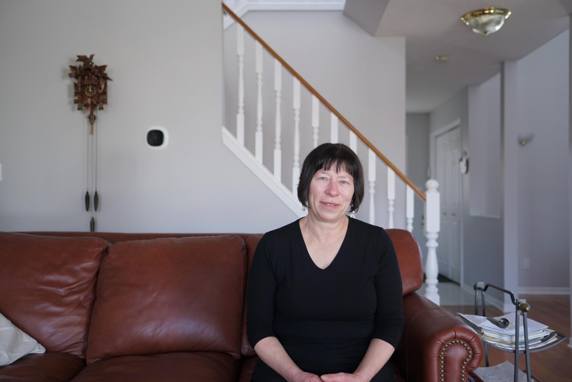 A woman with short, dark hair and a black shirt sits on a leather couch in her living room.