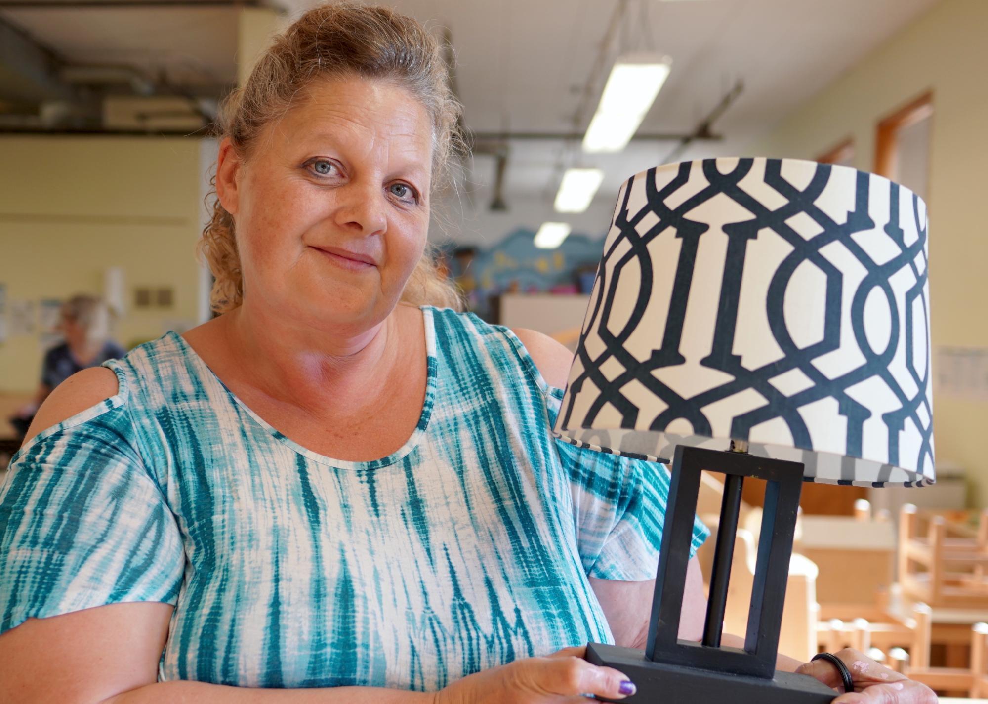 Woman with blue and white dress holds a refurbished lamp.