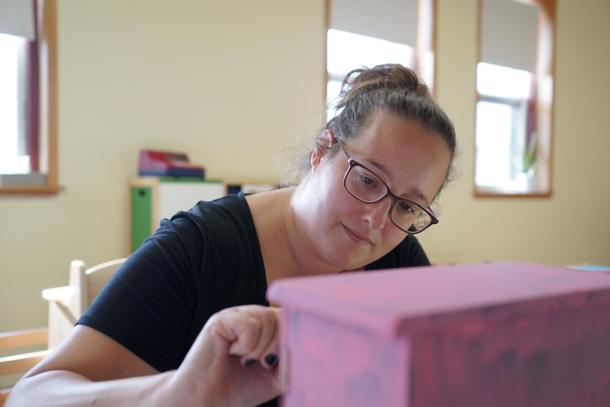 A woman with glasses and a black shirt works on a pink box