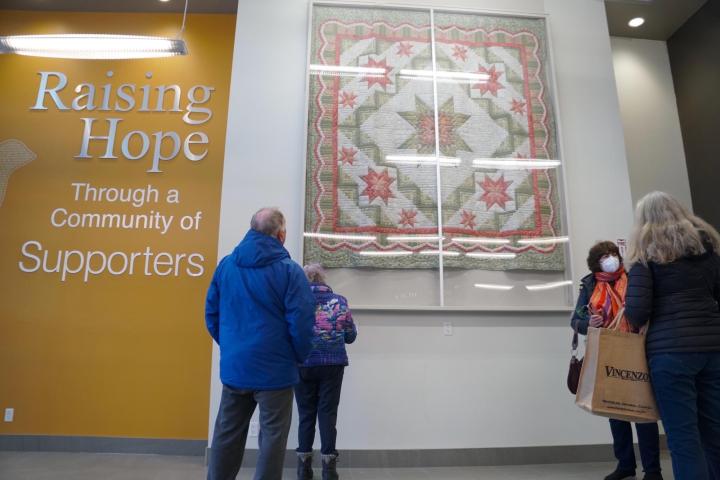 People looking at a hanging quilt