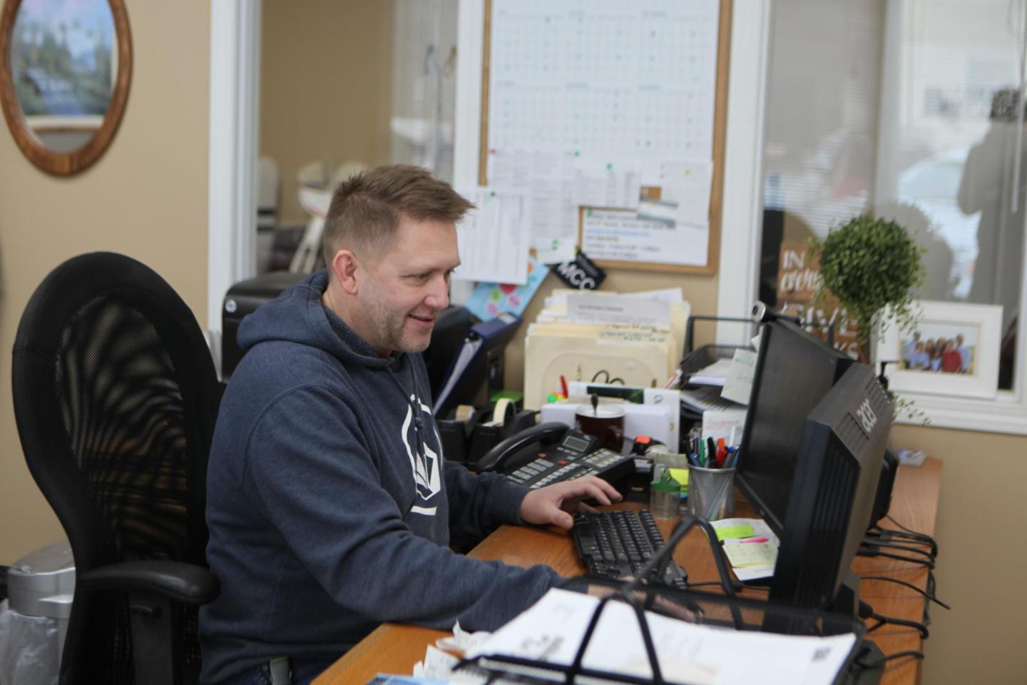 A man in a grey hoodie sits in front of a computer