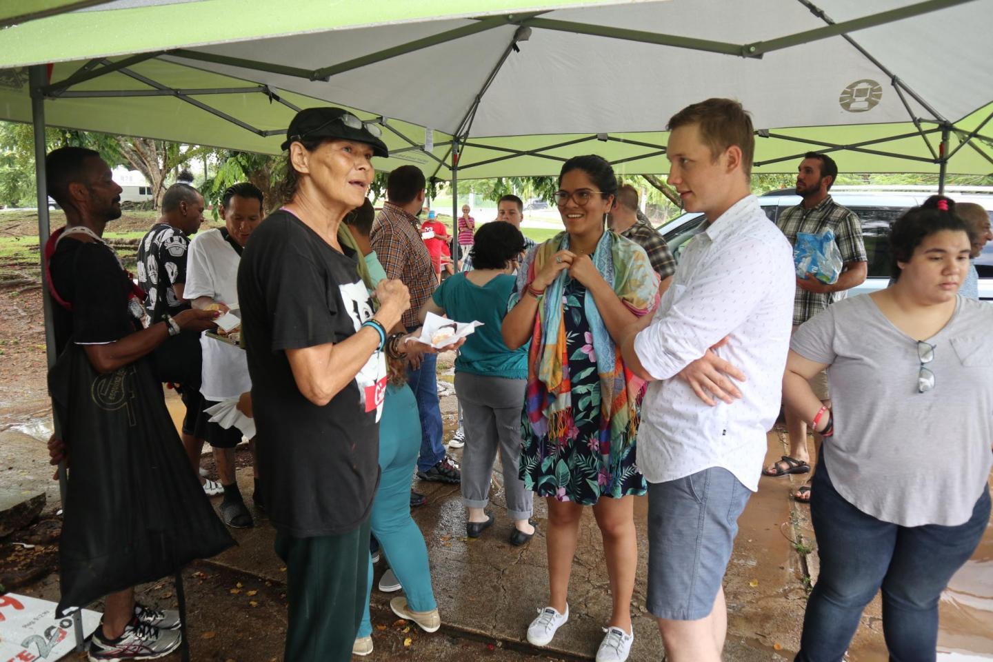 A group of people talk with one another outside underneath a tent canvas 