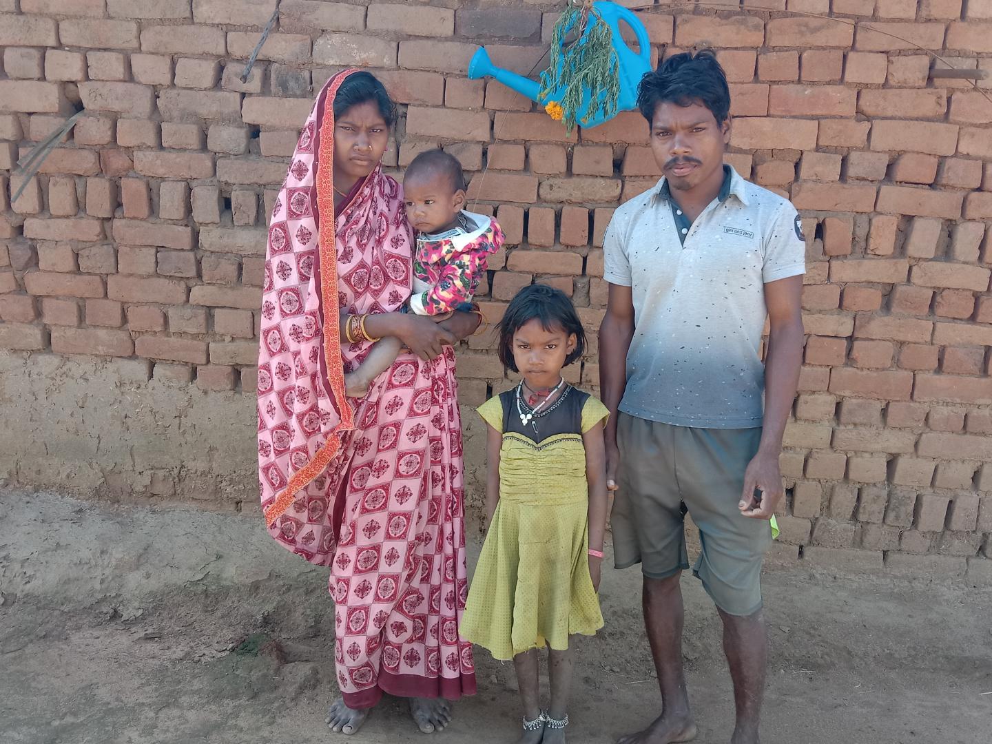 A family of four stand in front of a brick wall.