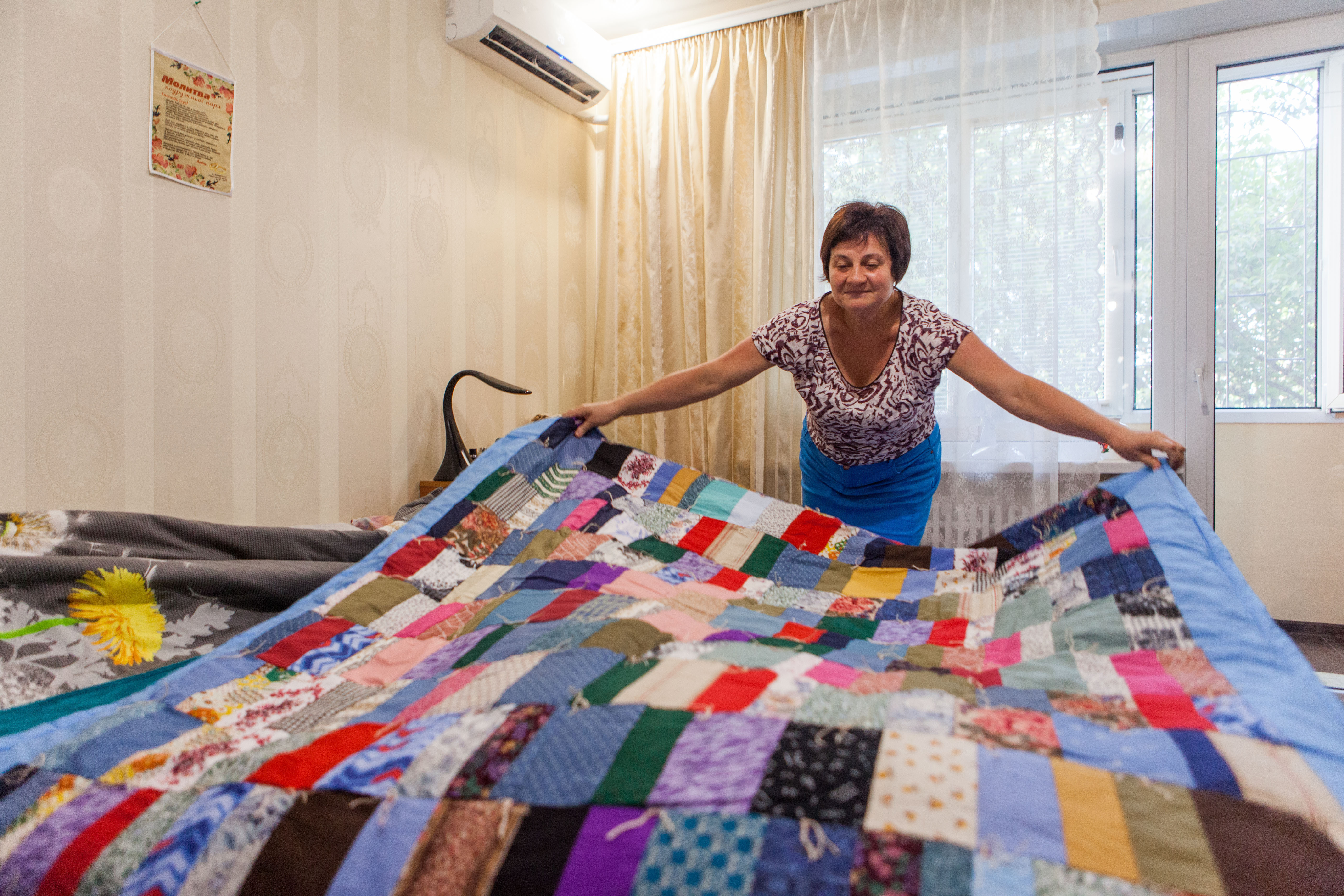 A Ukrainian woman places a colorful comforter over a bed