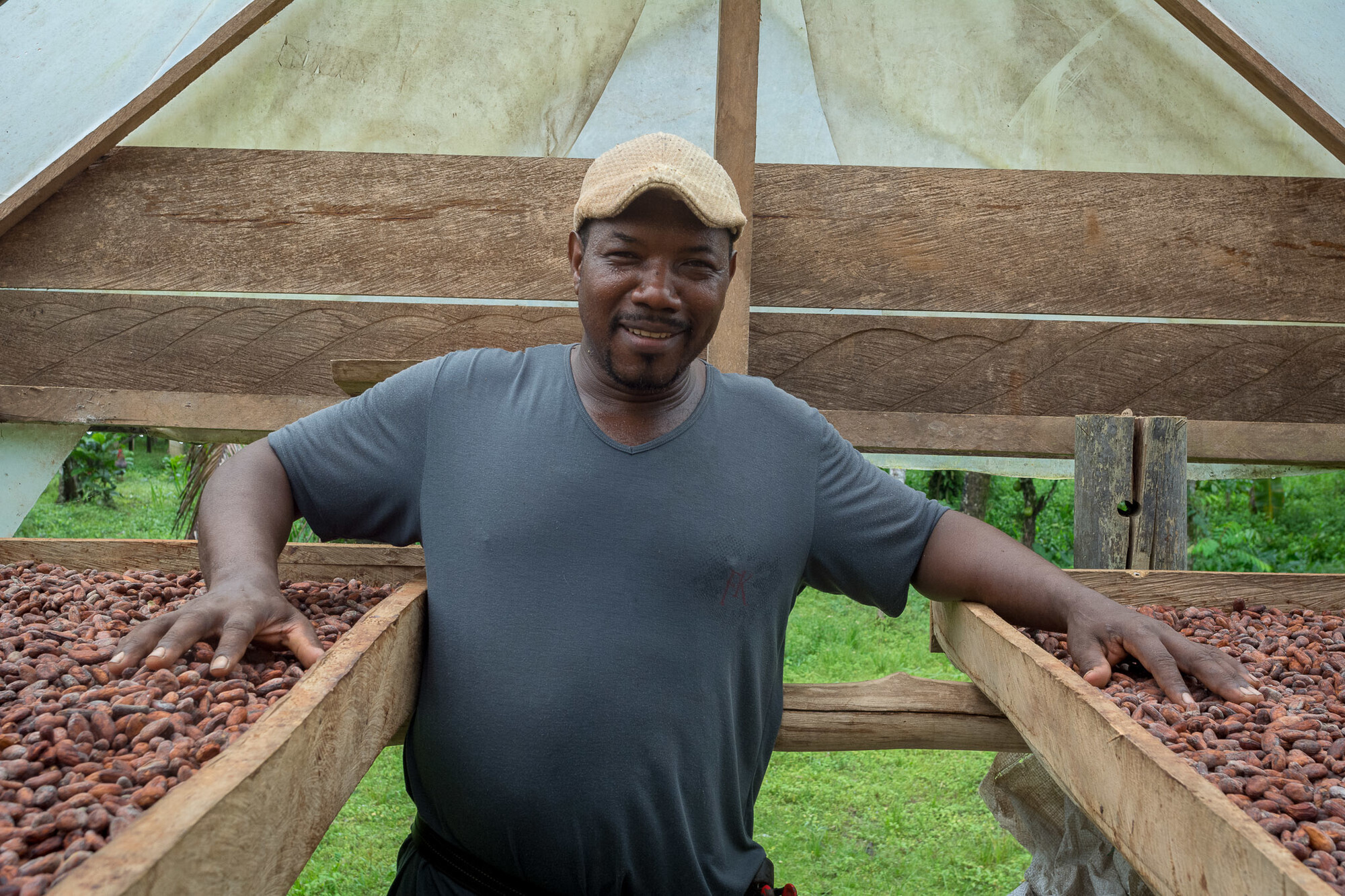 A man stands between two trays of cacao seeds