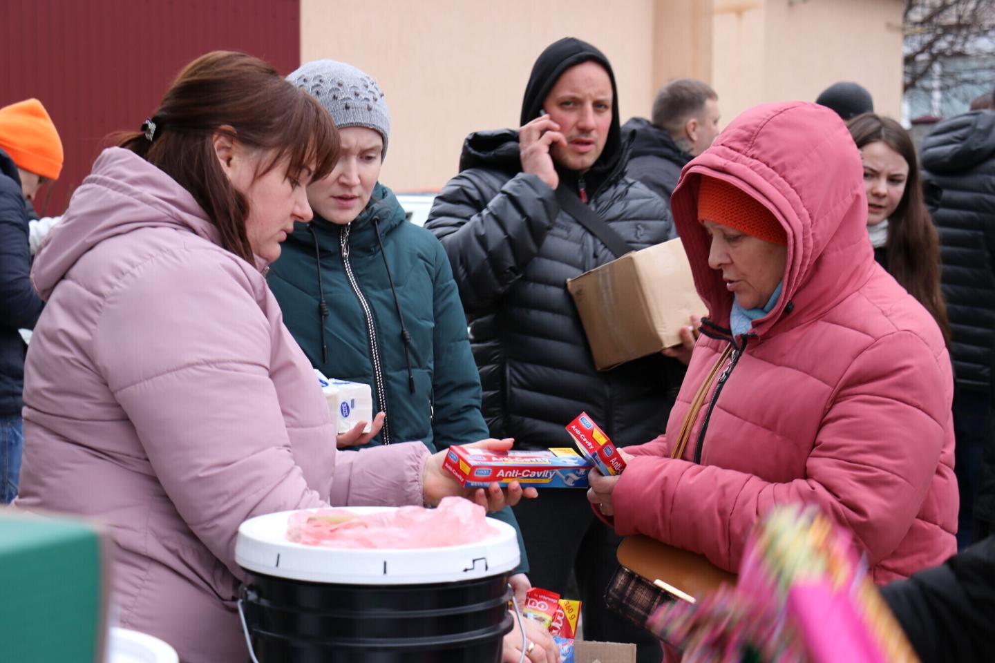 One woman hands another woman boxes of toothpaste. They are both wearing winter coats