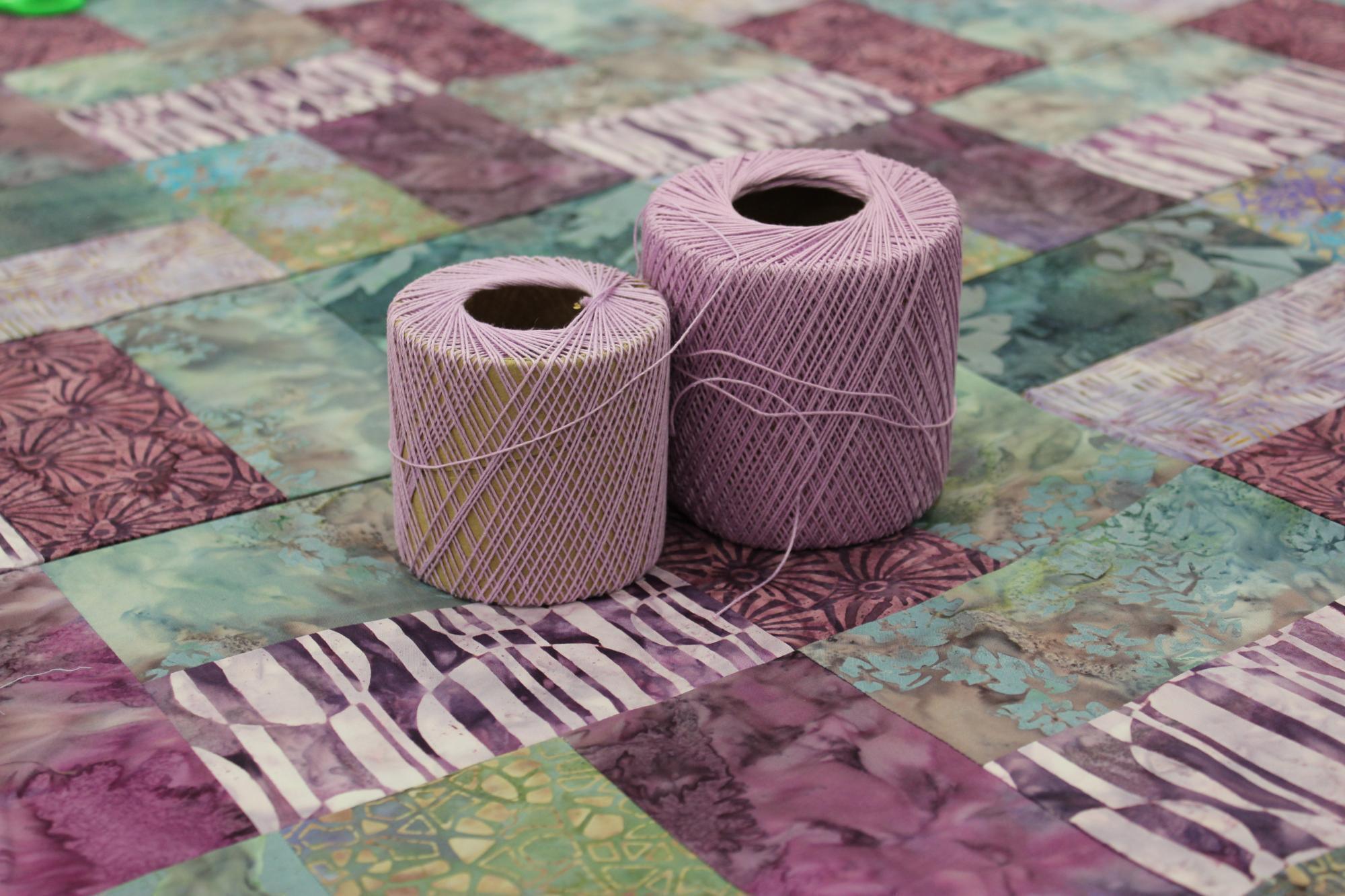 Two spools of purple yarn sit on top of comforter top