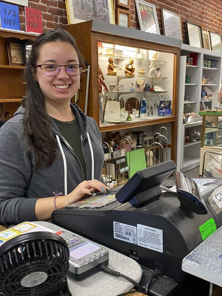 A young woman stands at the cashier station at a thrift shop