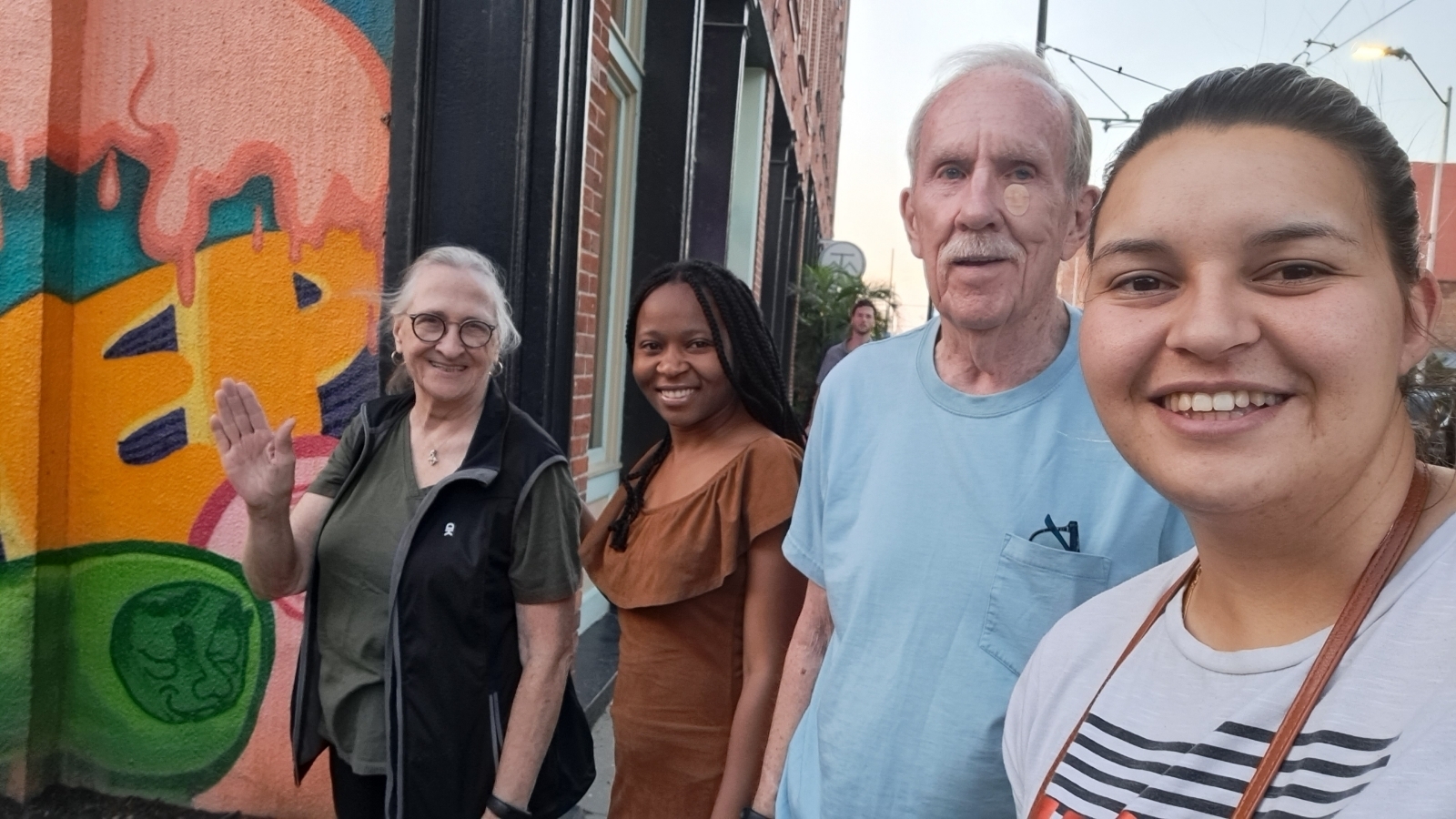 Two older people and two young adults stand together in front of a colorful building.