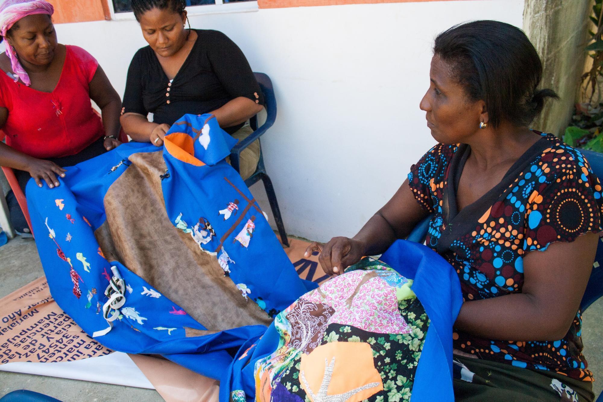 Three Colombia women sit and sew a comforter