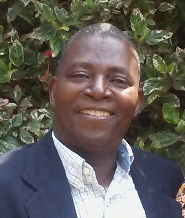 A  portrait of a man from the DR Congo. He is wearing a suit jacket and button down shirt.