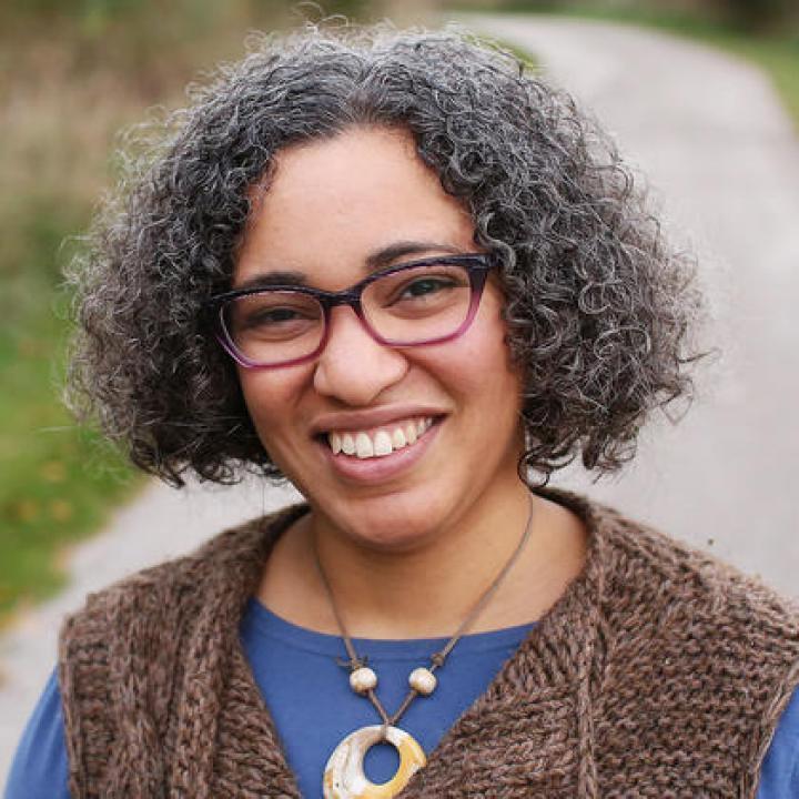 A woman with short grey curly hair, wearing purple glasses, stands in the middle of a path.