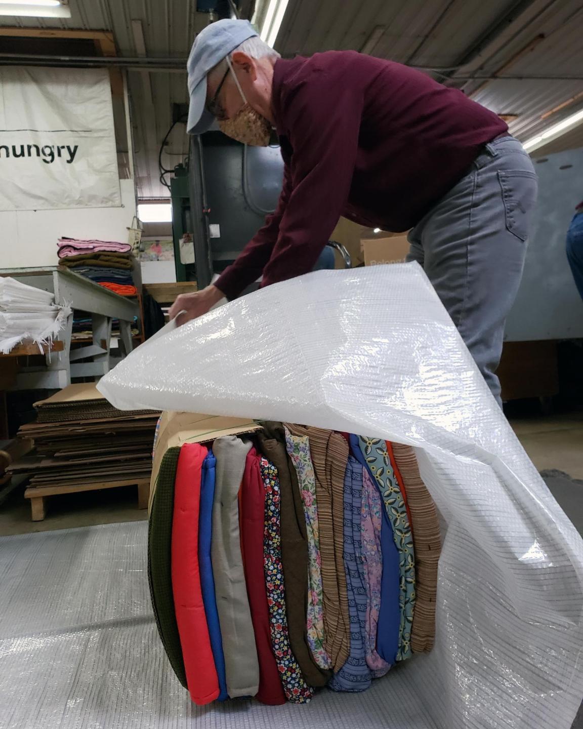 A man leans over a bale of comforters and wraps it in white plastic