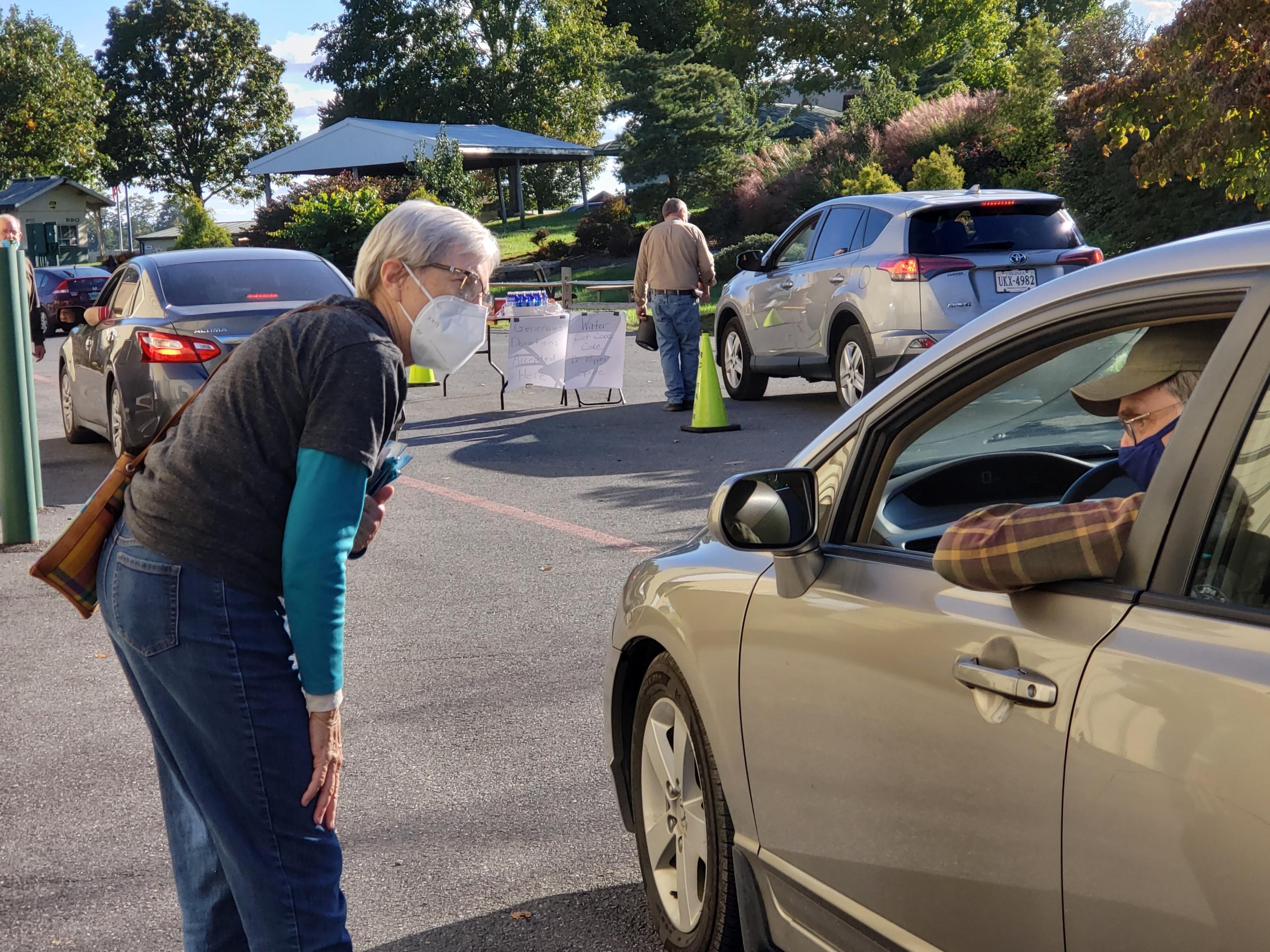 A woman wearing a mask talking to another person in a vehicle