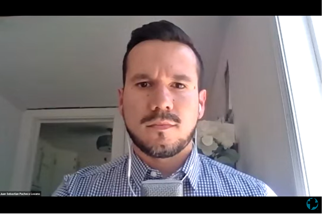 A young man with a beard and headphone speaks into the camera during a webinar on zoom