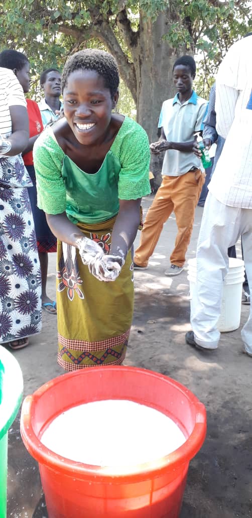 A Malawi woman washes her hands in a red, soapy bucket