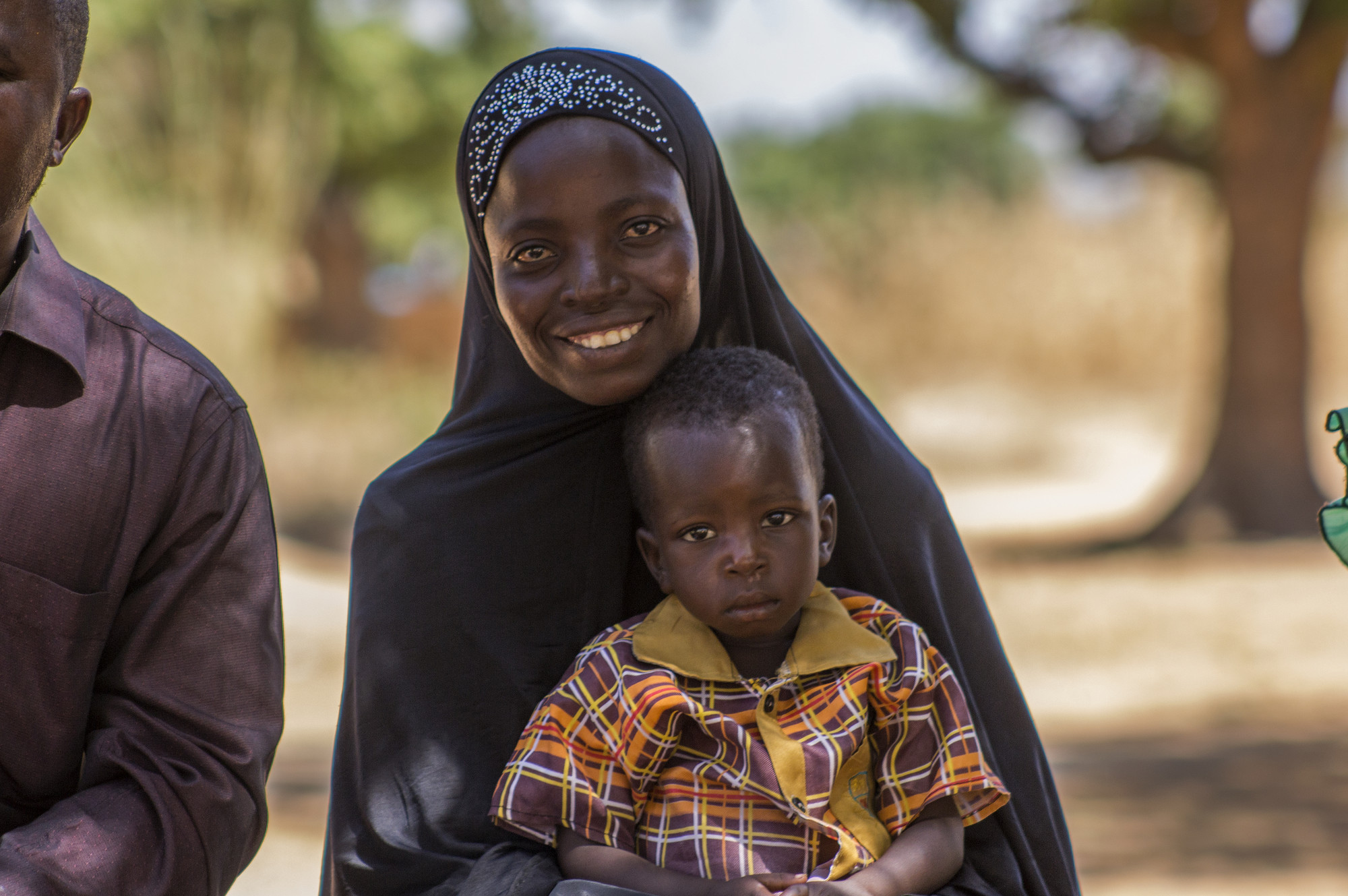 A woman in a hijab sits and holds her child in her lap