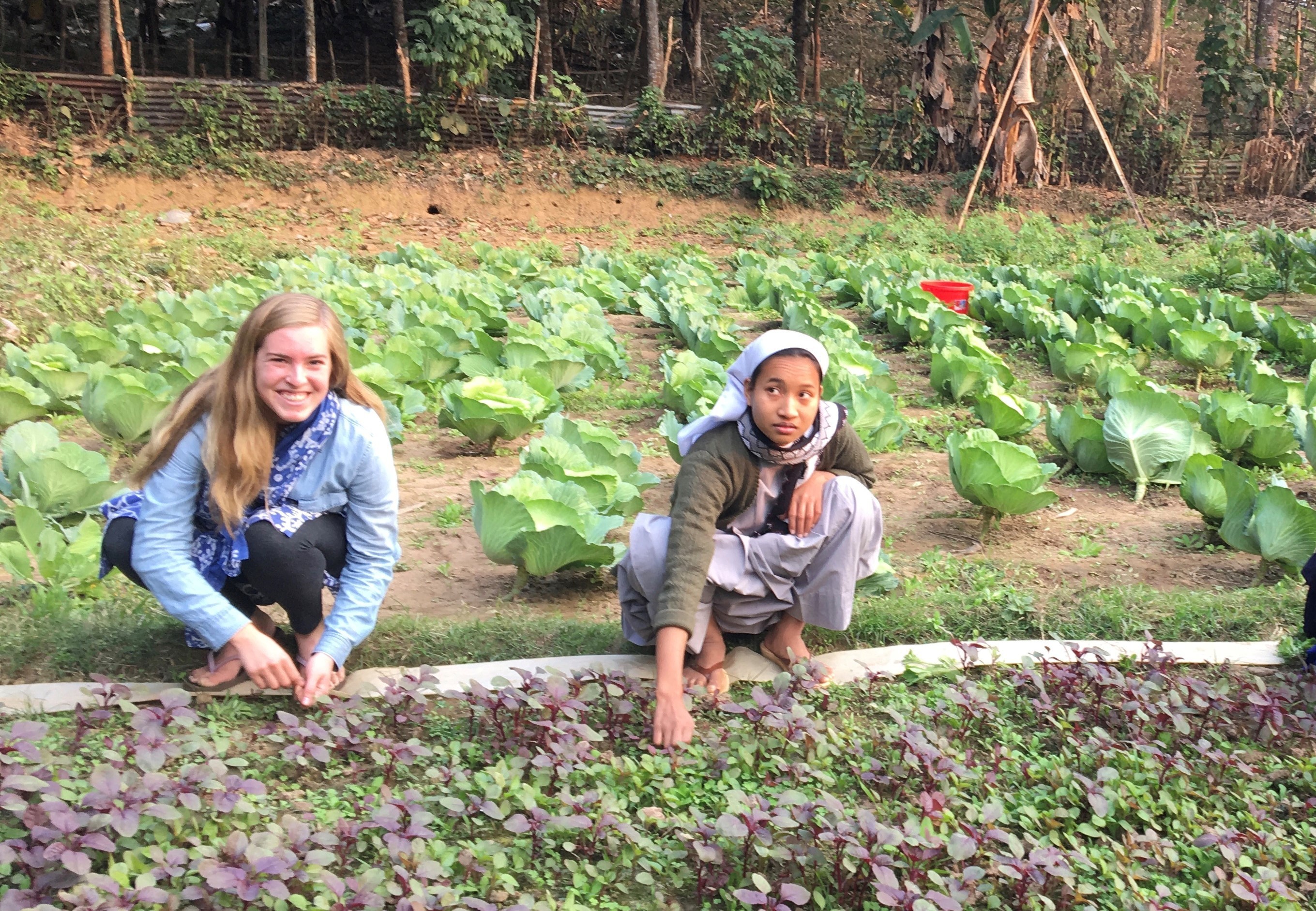 Two young women work to pull weeds in a garden