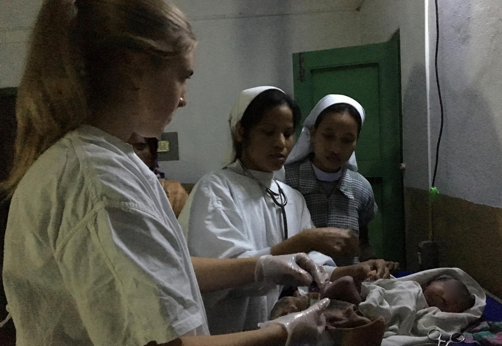 Three nurses in white work with a newborn baby