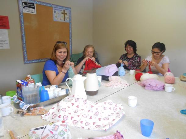 A group of four women sit at a table and crochet and knit