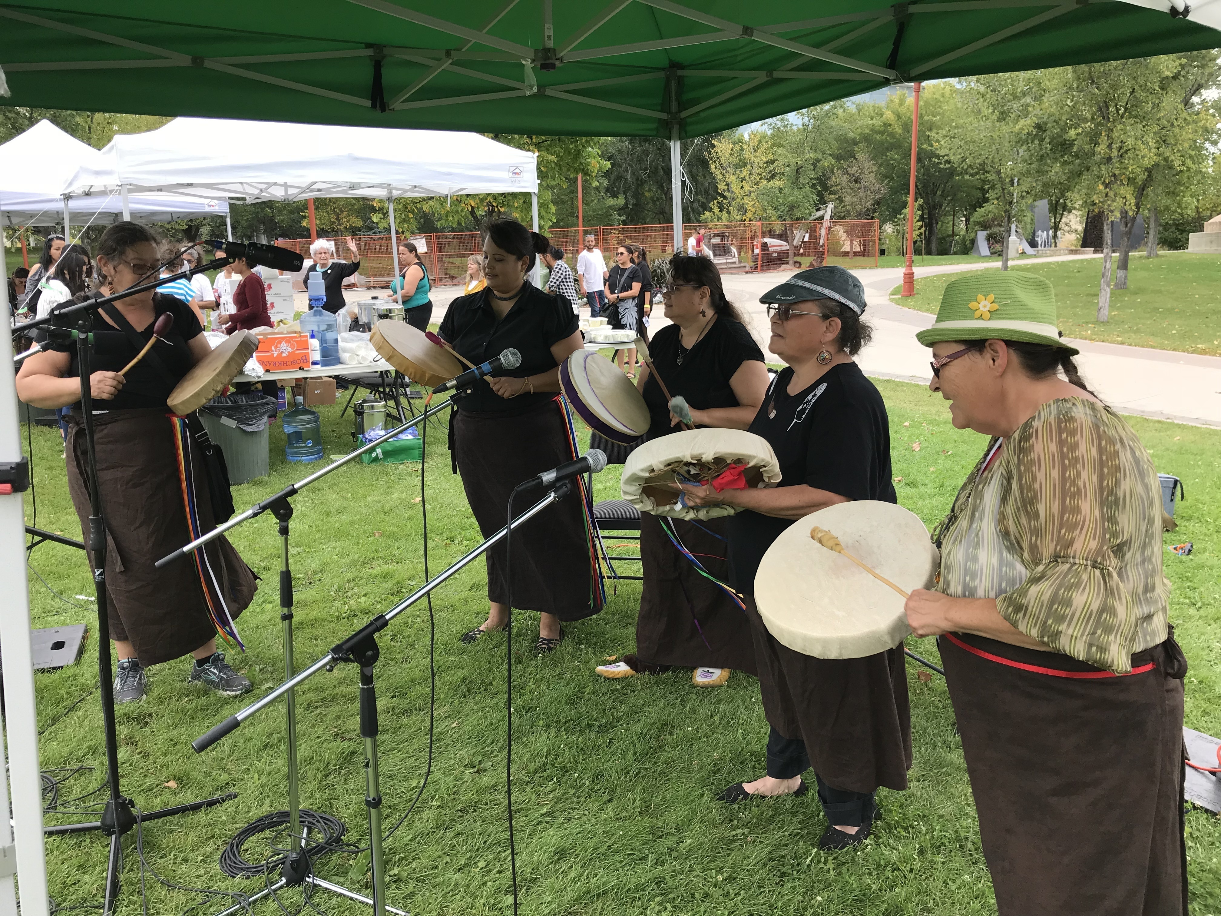 A group of Indigenous women play hand drums at an outdoor event