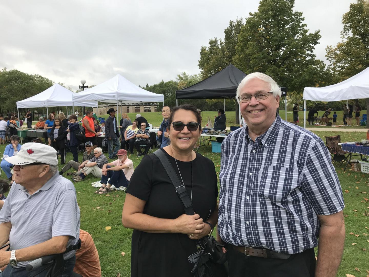 A woman in a black shirt and a man in a plaid shirt stand together at an outdoor event