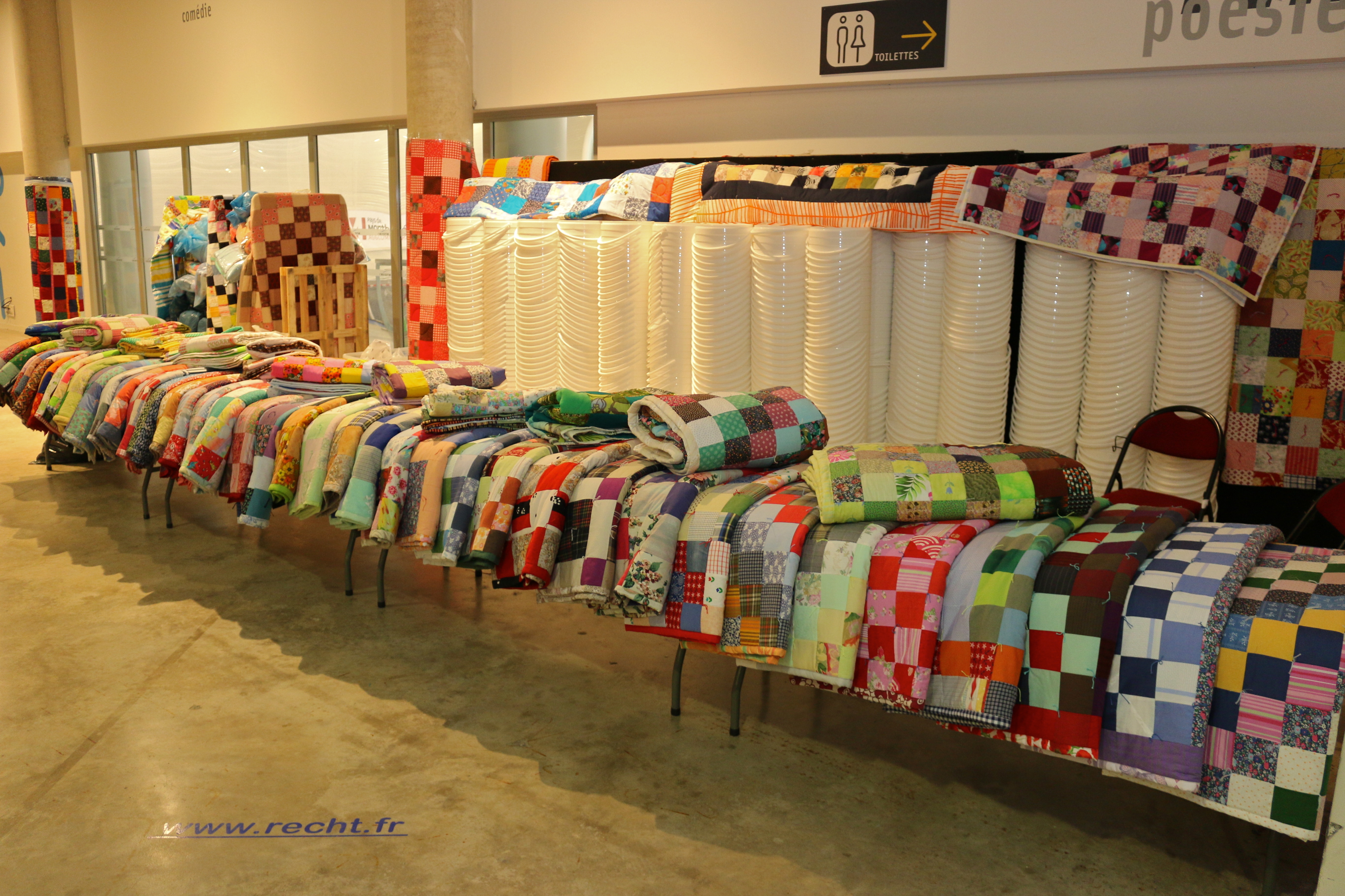 A large group of handmade comforters laid out on a long table