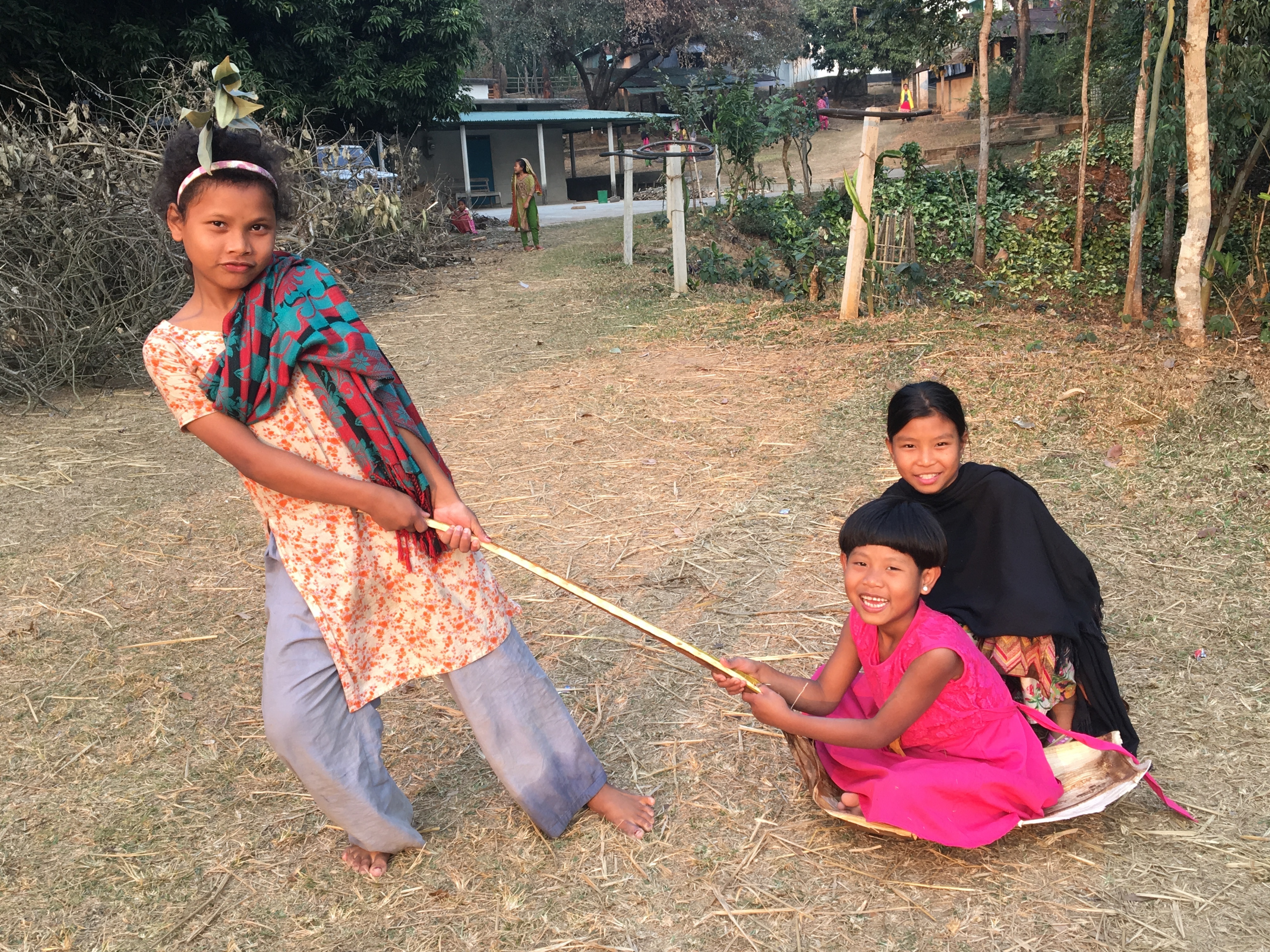 Three child play together. One child is pulling another in a makeshift sled