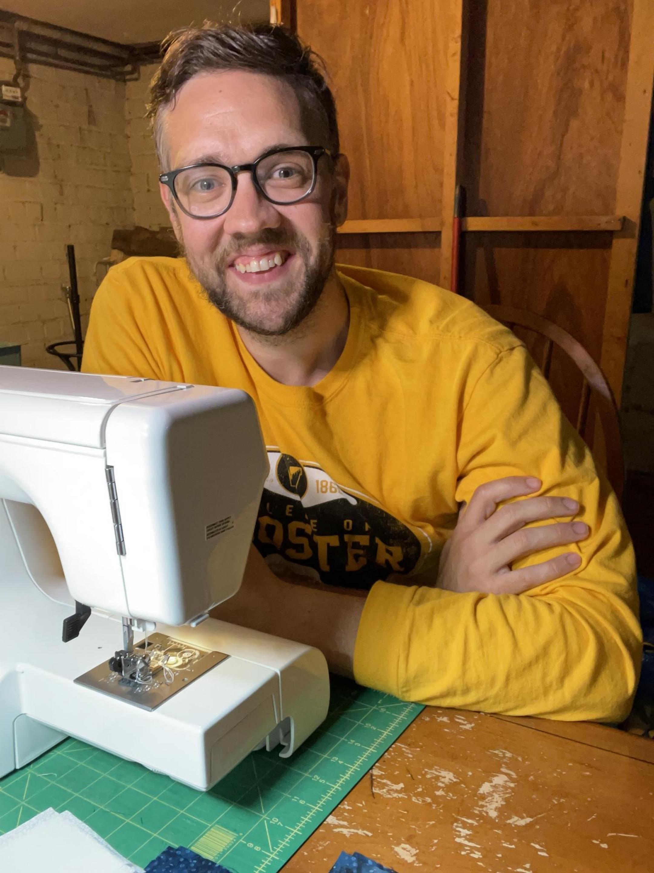 Paul smiling for a photo by his sewing machine