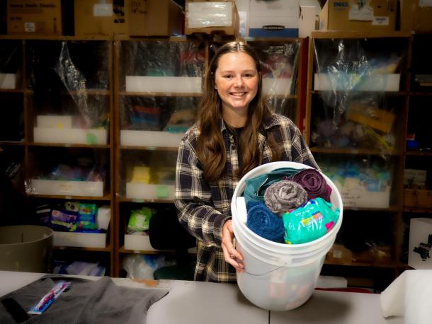 A young woman stands and holds a bucket full of colorful towels