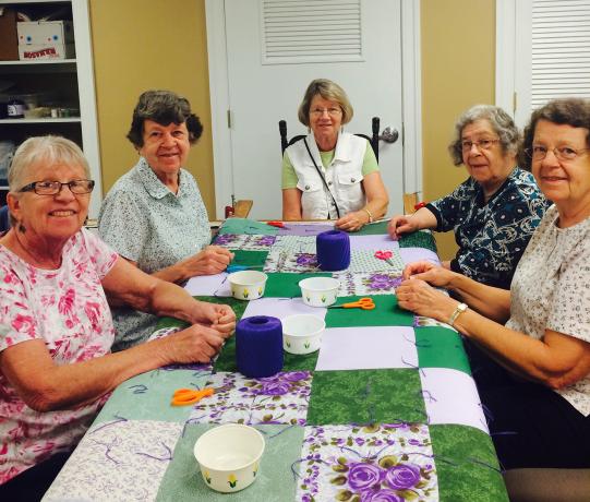 5 women sit around and work on a comforter top