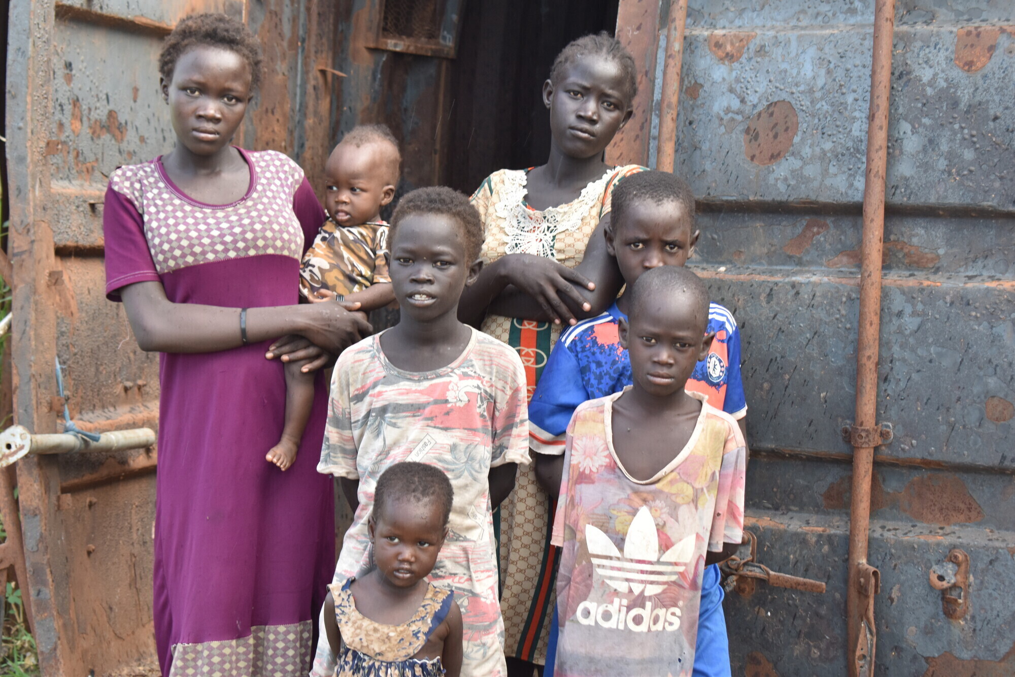 A group of young children stand in front of a shipping container