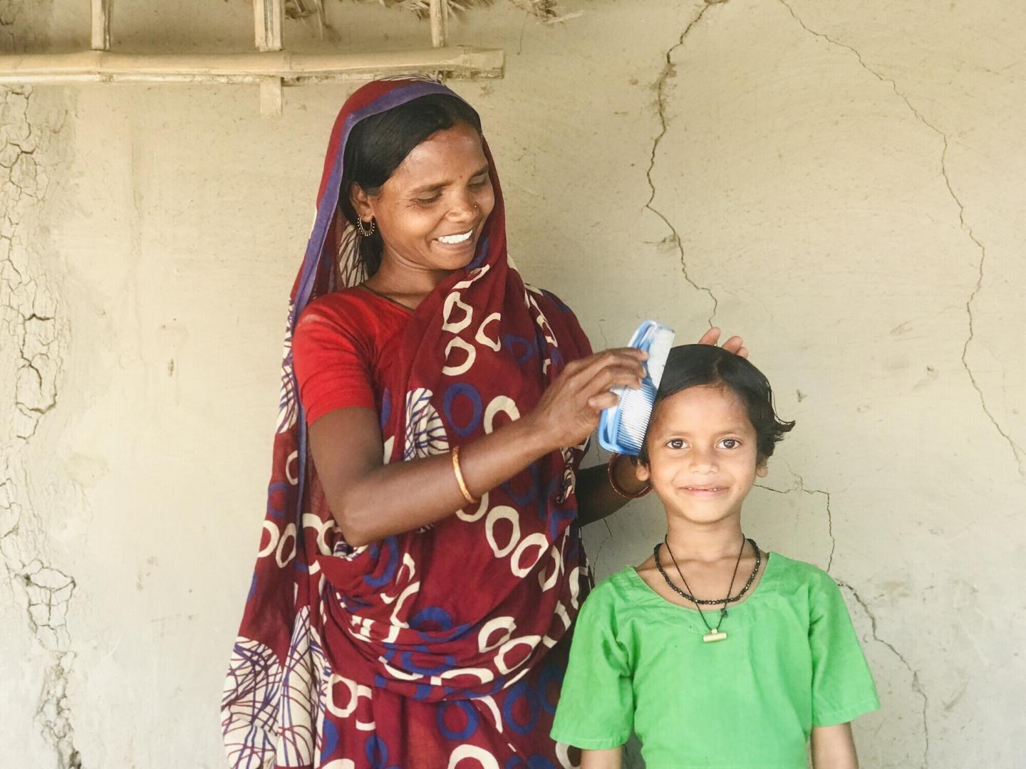 A Bangladeshi woman combs the hair of a child in a green shirt