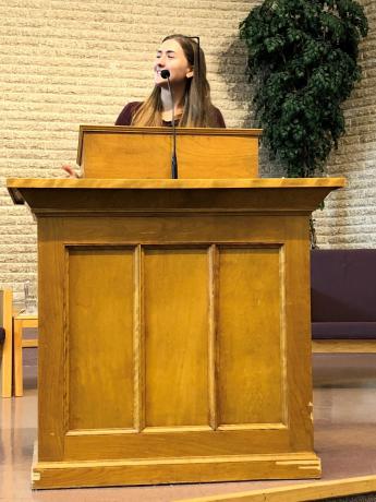 A young woman stands behind a large wooden pulpit at a church