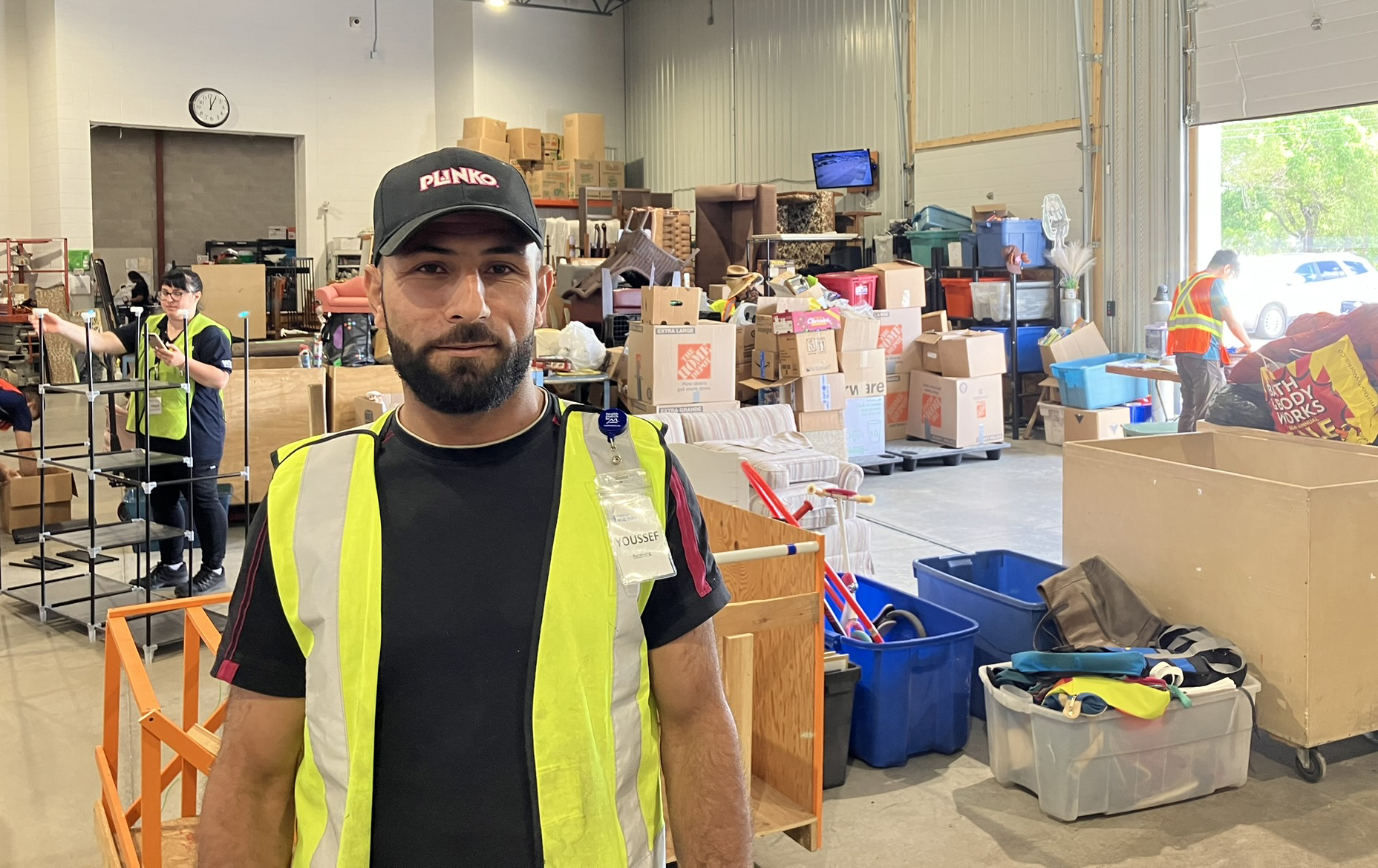 A man in a high-visibility vest stand in front of a warehouse full of boxes