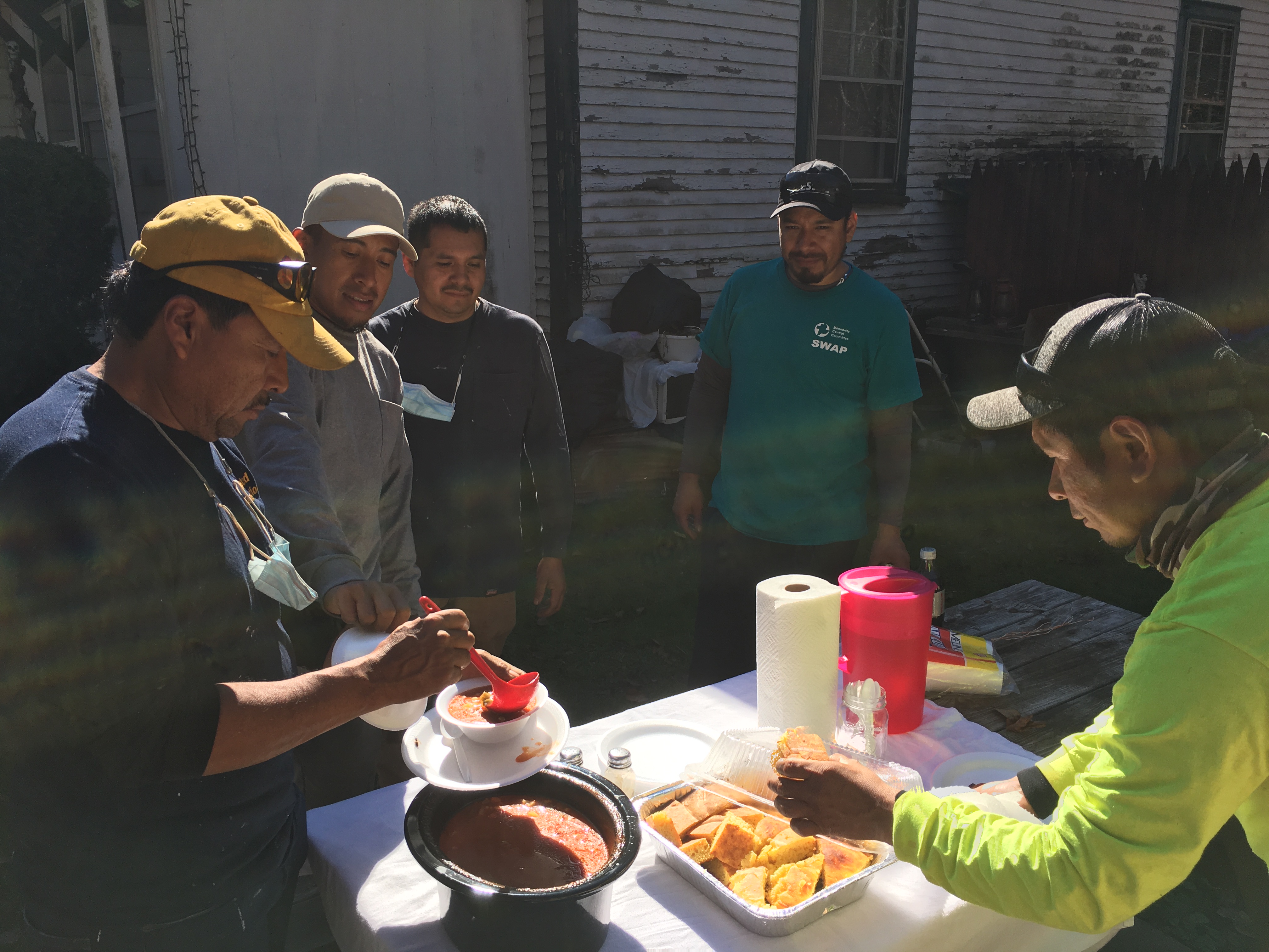 people stand around table and scoop soup from bowl