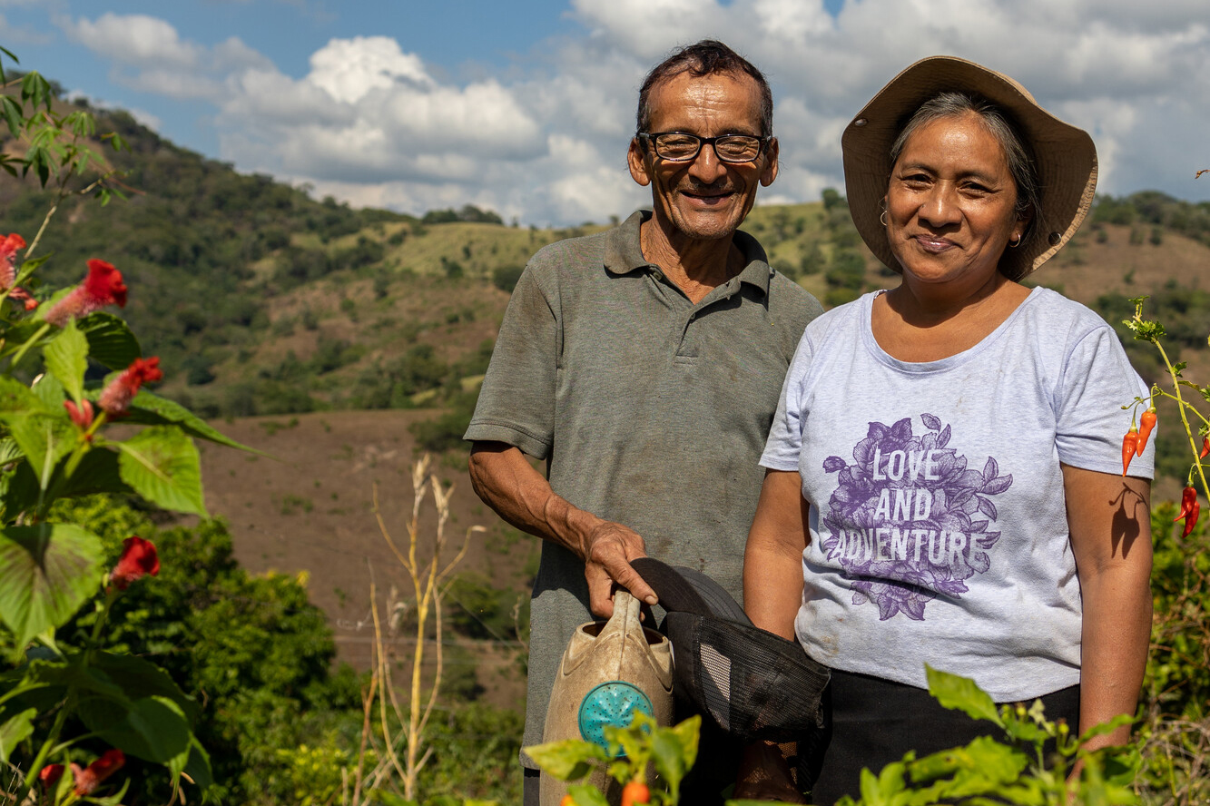 Two people stand in a field with mountains in the background