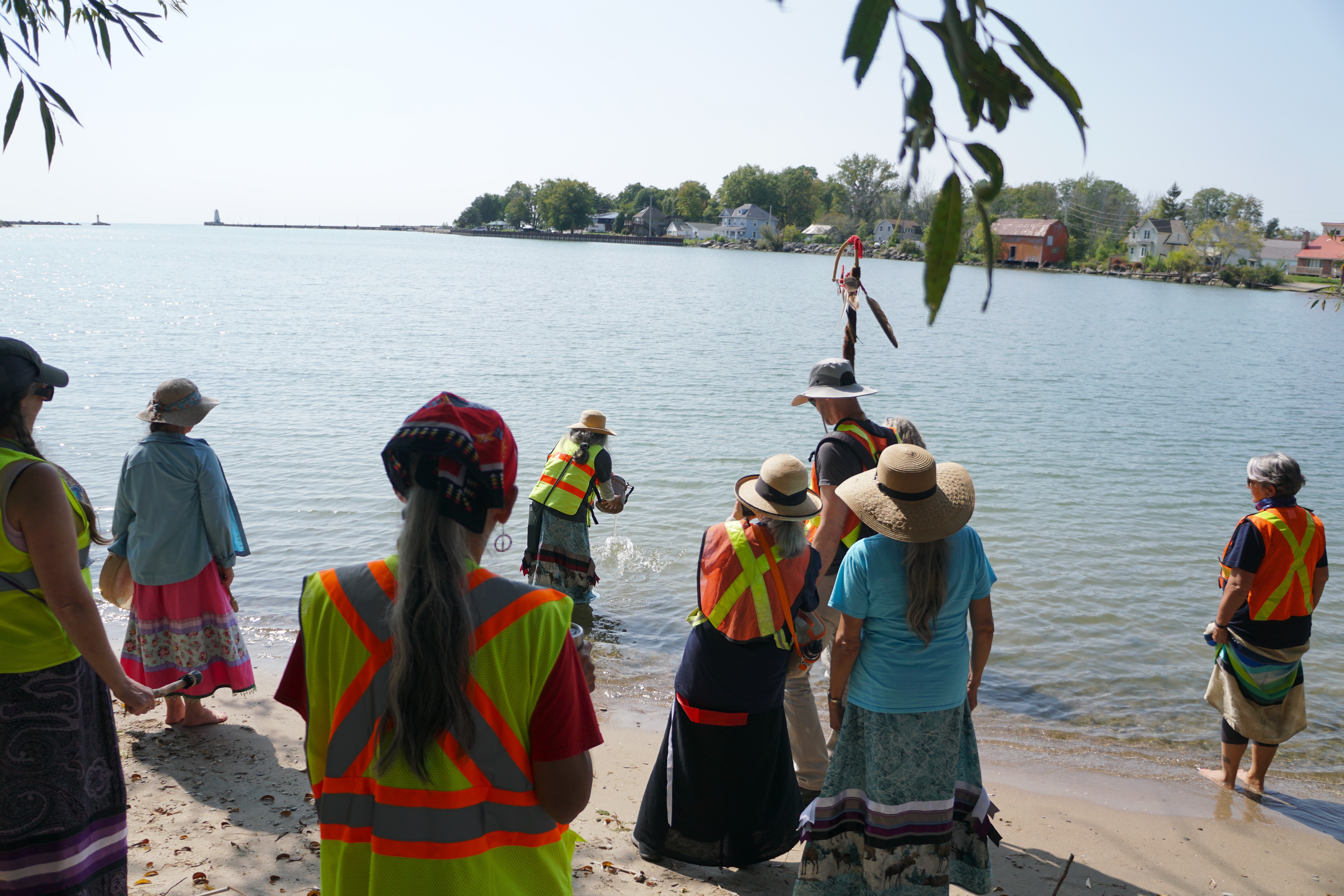 Group of people at beach watching woman pour water into the lake