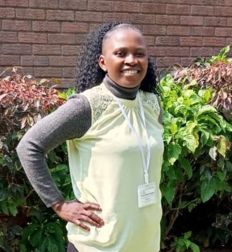 Woman standing outside near bushes with hands on hips.