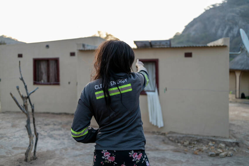 A woman pointing to a solar panel of the roof of a small house